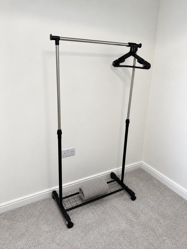Empty bedroom with black metal clothing rail and single hanger on carpet