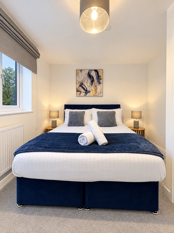 Modern bedroom with double bed, navy bedding, white pillows, bedside lamps and framed artwork