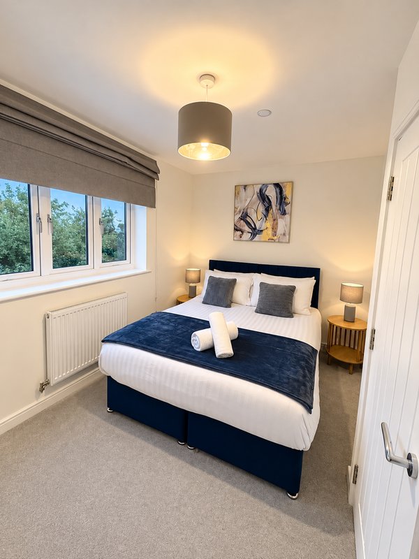 Modern bedroom with double bed, navy bedding, bedside lamps, and large window with grey blinds
