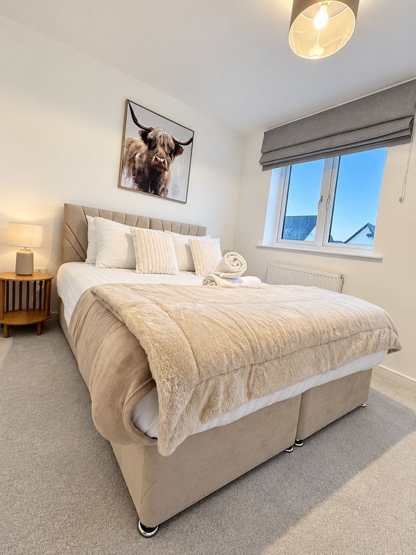 Bright modern bedroom with grey upholstered bed, cream bedding, framed wall art, and large window with mountain view