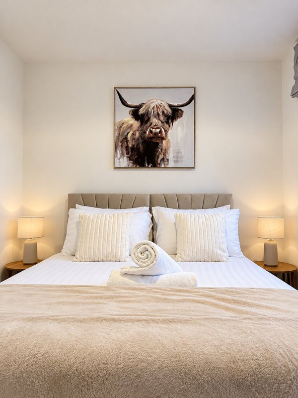 Modern bedroom with double bed, grey headboard, white pillows, bedside lamps and wall art