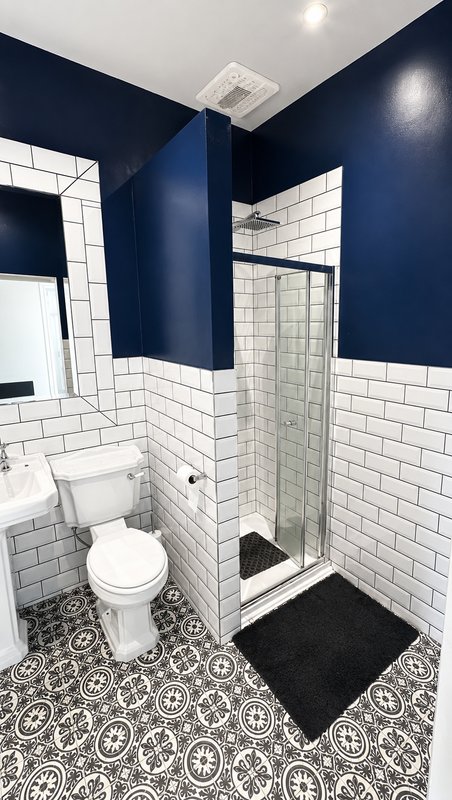 Modern bathroom with navy blue walls, white subway tiles, glass shower enclosure, toilet and patterned floor