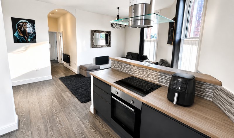 Modern open-plan kitchen and living area with wooden countertops, black appliances, and contemporary furnishings