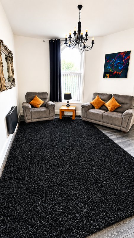 Bright living room with two grey sofas, black chandelier, black rug and yellow cushions