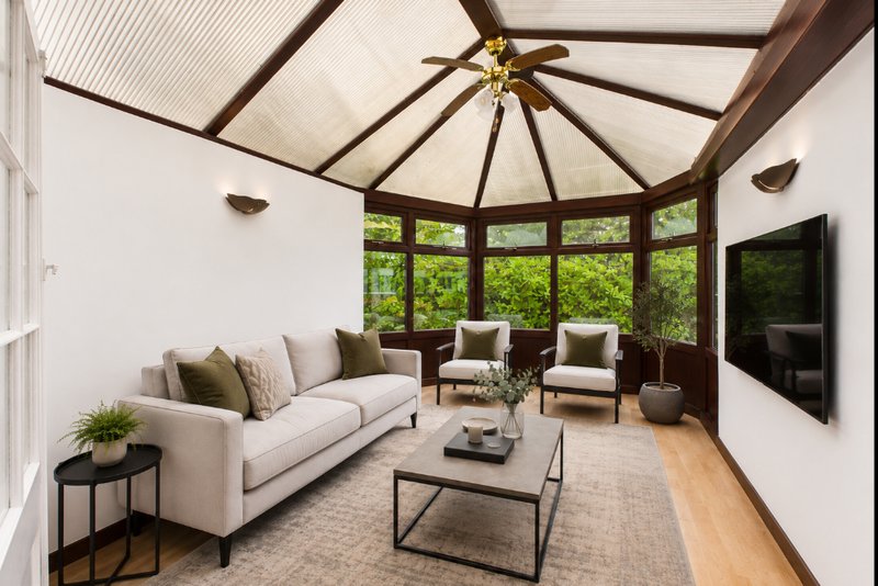 Modern conservatory with cream sofa, armchairs, coffee table and wall-mounted TV