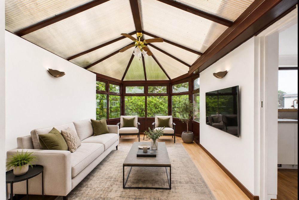 Bright conservatory with cream sofa, wooden beams, skylight roof and garden views