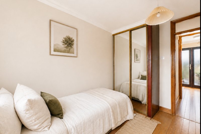 Bright bedroom with single bed, white bedding, wooden wardrobe, and framed wall art