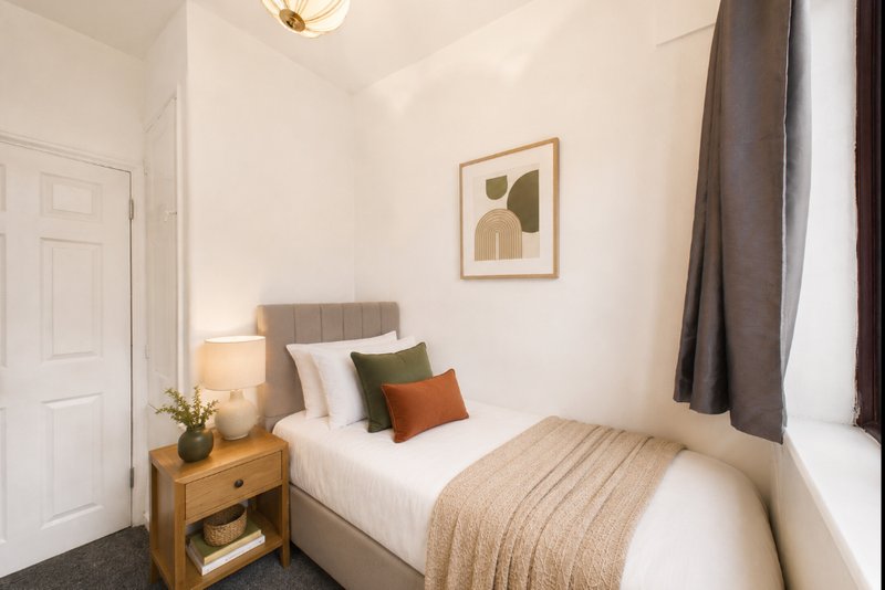 Bright bedroom with single bed, wooden nightstand, framed wall art and curtains