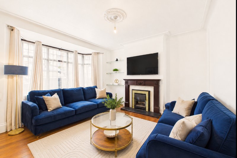Bright living room with two blue sofas, fireplace, wall-mounted TV, and round coffee table