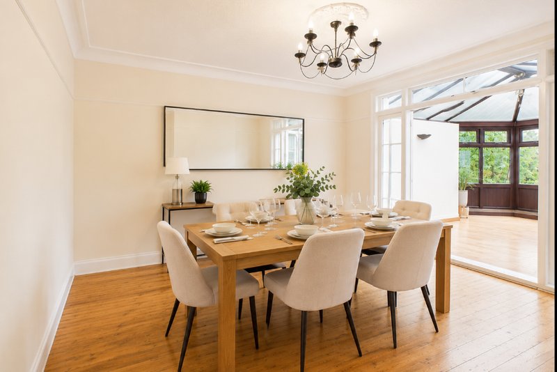 Bright dining room with wooden table, cream chairs, mirror, and pendant light fixture