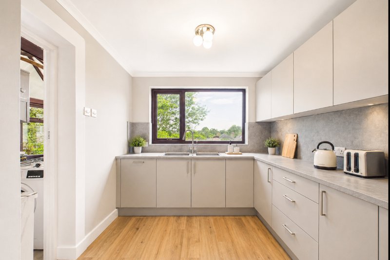 Modern kitchen with cream cabinetry, wooden flooring, window overlooking garden, and stainless steel appliances