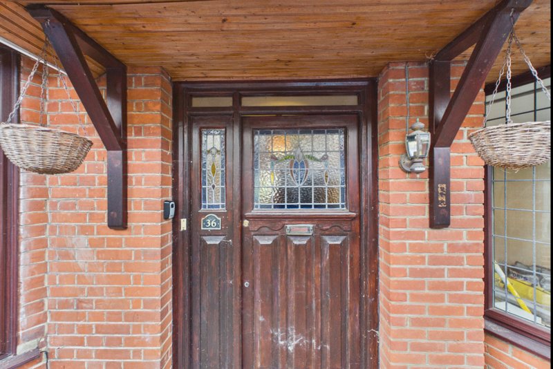 Traditional brick cottage entrance with dark wooden door, glazed panels, and hanging baskets
