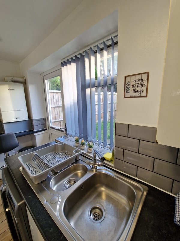 Kitchen with double sink, black subway tile splashback, vertical blinds and garden view