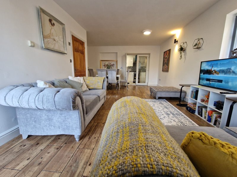 Open-plan living room with sofa, TV, wooden floor, rug and kitchen entrance