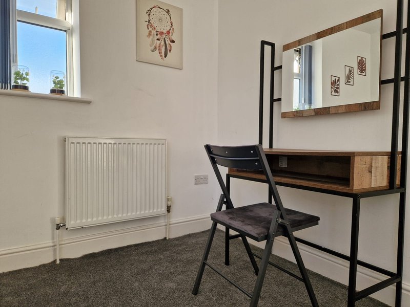 Bedroom with desk, black chair, radiator, window and wall-mounted mirror