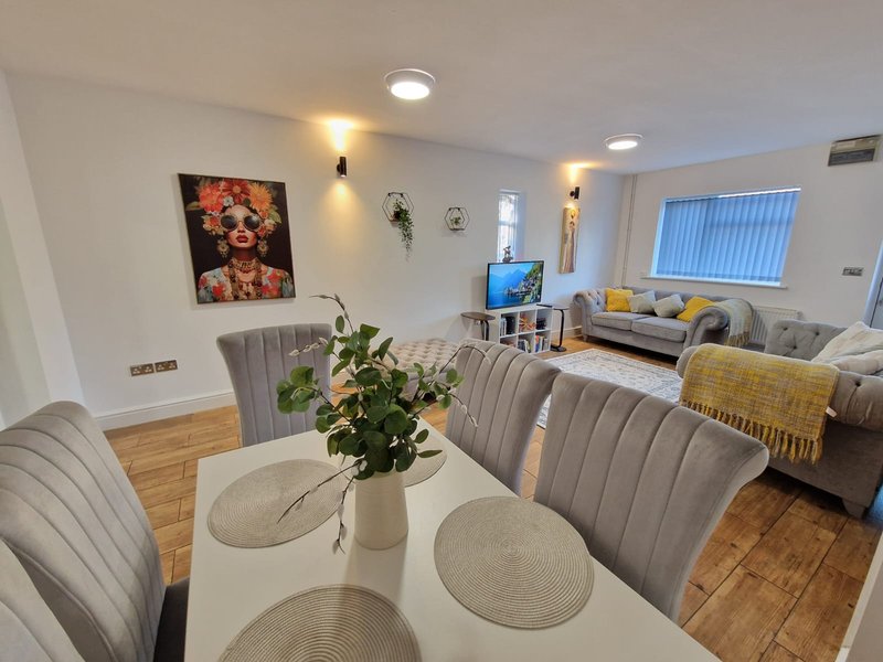 Open-plan living and dining area with grey upholstered chairs, white table, sofa, and artwork on wall