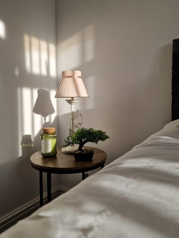 Bedroom bedside table with lamp, small plant, and candle in natural light