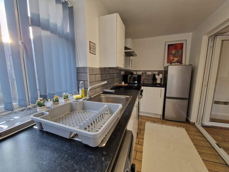 Kitchen with white units, stainless steel fridge, sink with dish rack, and window with vertical blinds