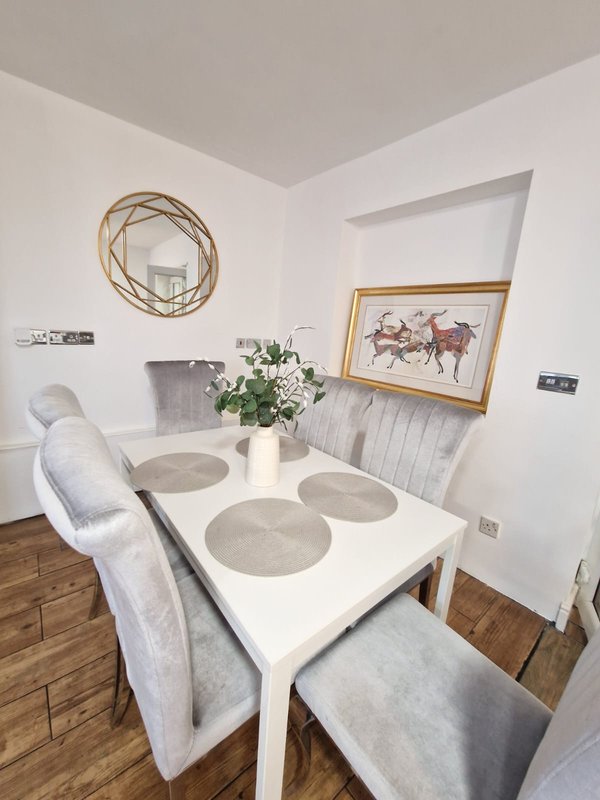Modern dining area with white table, upholstered chairs, wooden floor and wall art