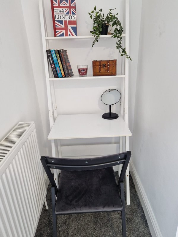 Small corner nook with white shelving, black chair, books, plant and decorative items
