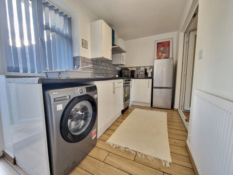 Modern kitchen with white cabinets, black washing machine, stainless steel appliances and wooden flooring
