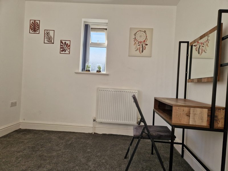 Bright bedroom with window, radiator, framed wall art, folding chair and shelving unit