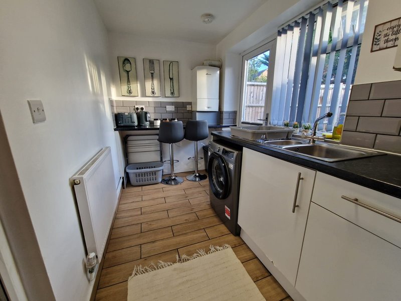 Galley kitchen with white cabinets, black countertop, washing machine and sink