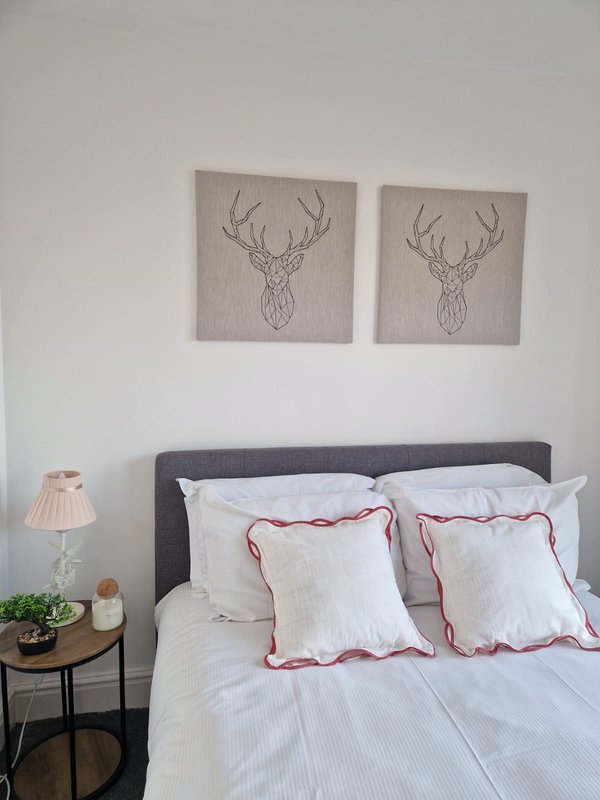 Bedroom with double bed, decorative deer artwork above headboard, bedside table and lamp