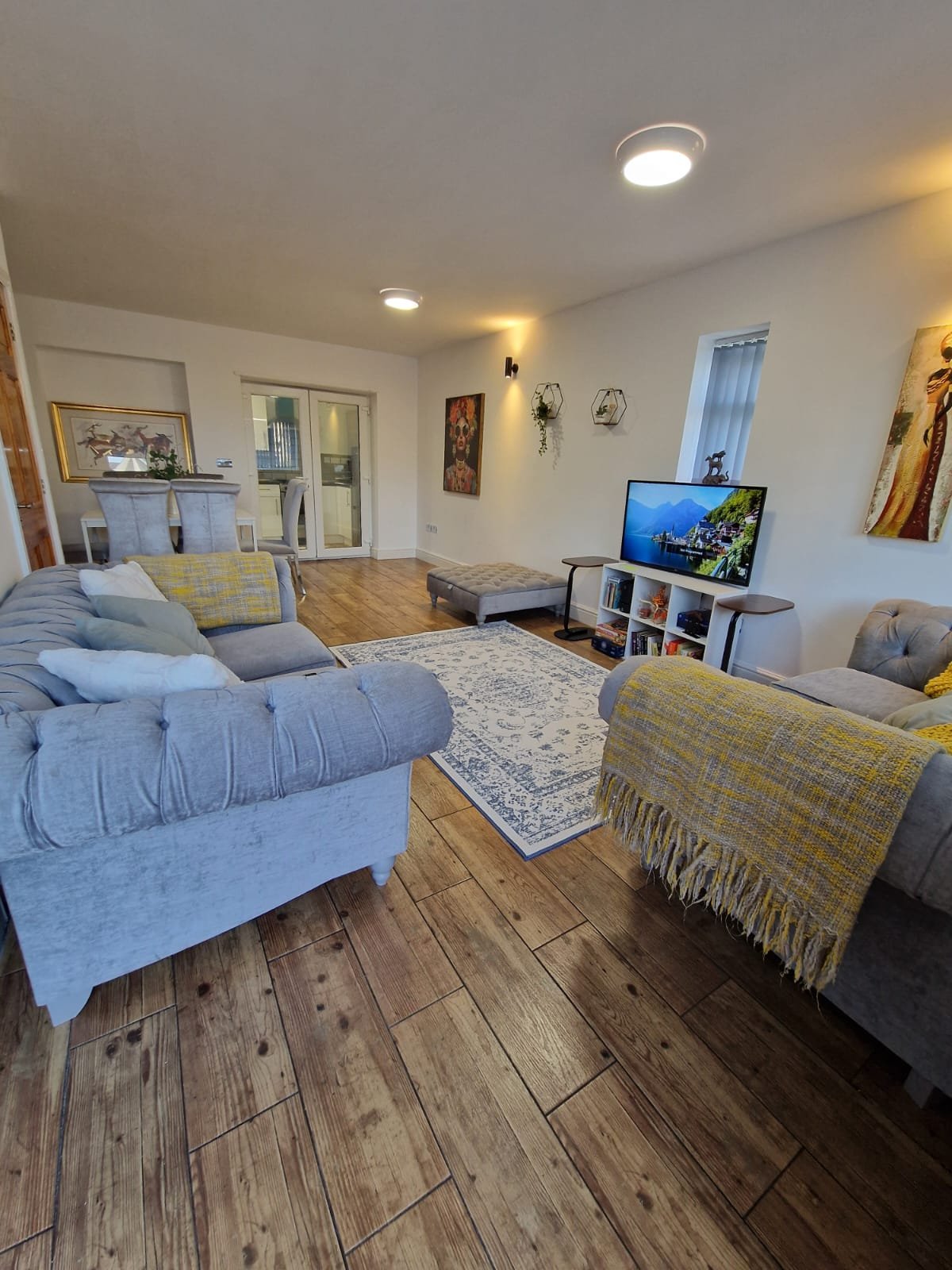 Open-plan living area with sofa, armchair, TV, wooden flooring and recessed ceiling lights