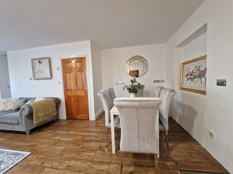 Open-plan living and dining area with wooden flooring, upholstered seating, and framed wall art