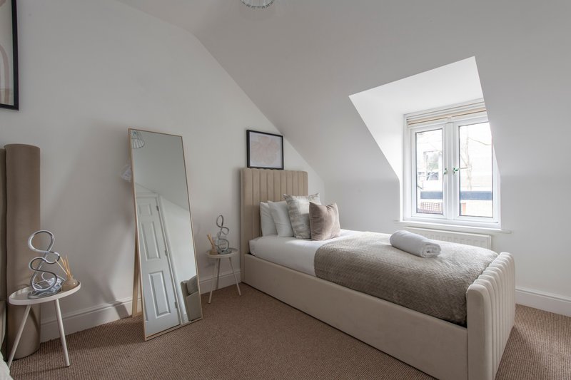 Bright attic bedroom with single bed, skylight window, mirror and neutral decor