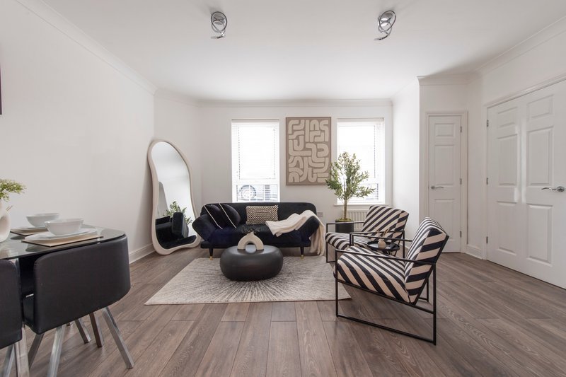 Spacious modern living room with black sofa, zebra-striped chair, round ottoman, wooden flooring and white doors