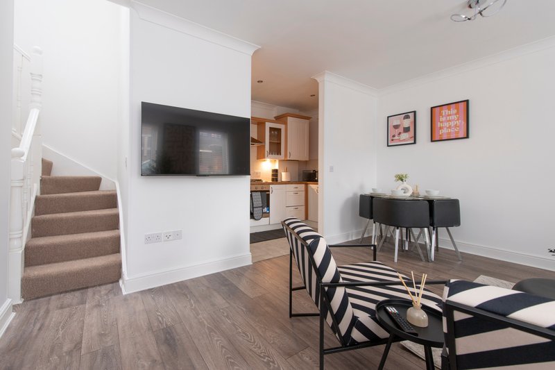 Open-plan living area with stairs, wall-mounted TV, dining table and kitchen visible
