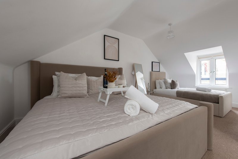 Modern bedroom with brown upholstered bed, white bedding, and neutral furnishings in bright space