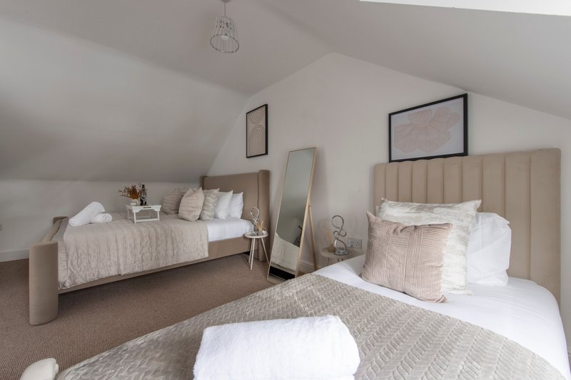 Bright attic bedroom with two single beds, neutral bedding, wooden headboards and pendant lighting