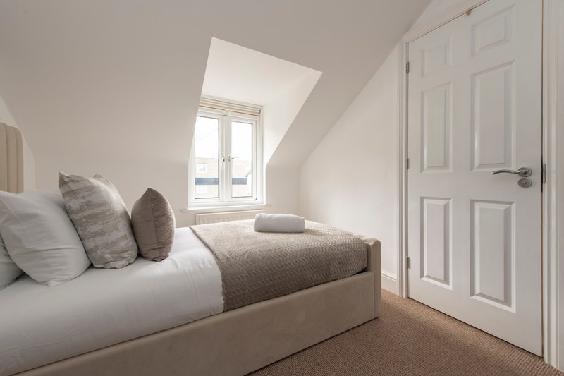 Modern bedroom with made bed, decorative pillows, skylight window, and white door
