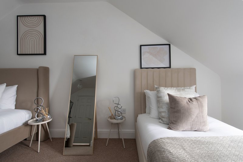 Modern bedroom with two beds, mirrors, framed wall art, and neutral furnishings