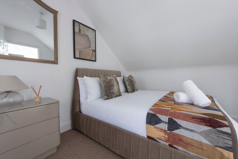 Modern bedroom with double bed, cushions, wooden headboard and neutral decor