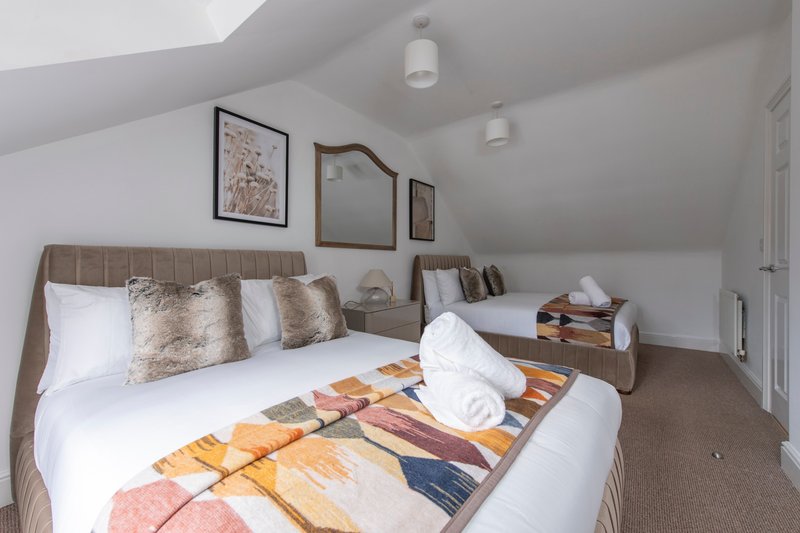 Bright attic bedroom with two single beds, neutral bedding, framed wall art and sloped ceiling
