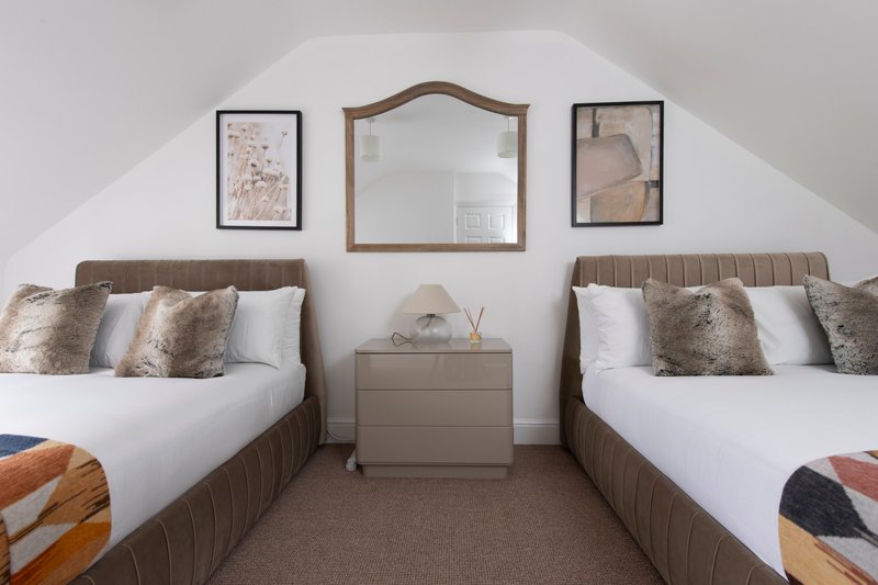 Twin bedroom with two beds, neutral bedding, framed wall art, and central mirror in sloped ceiling room