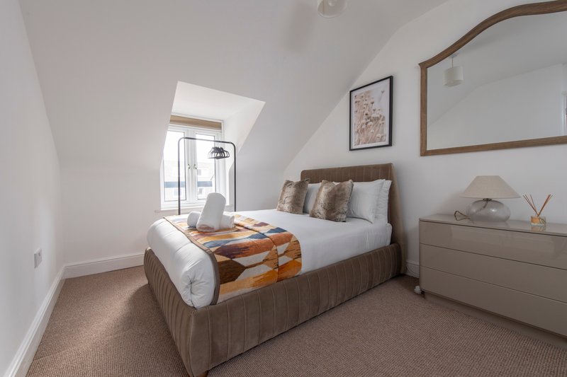 Bright bedroom with double bed, wooden headboard, orange throw and skylight window