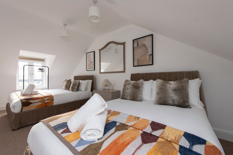 Bright attic bedroom with two double beds, white bedding, cushions and geometric patterned throw blankets