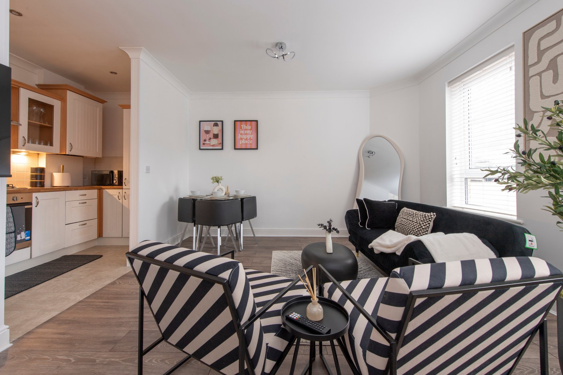 Modern open-plan living room with striped armchairs, black side table, and kitchen visible on left
