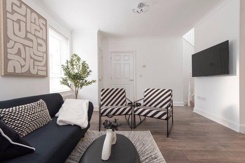 Modern living room with black sofa, striped armchairs, wall-mounted TV and decorative artwork