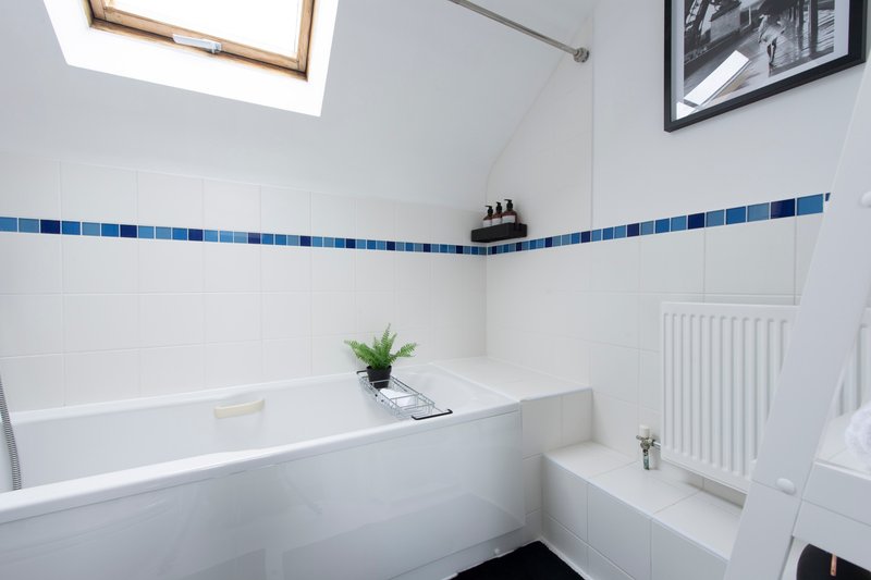 Modern bathroom with white bathtub, blue tile border, skylight window and radiator