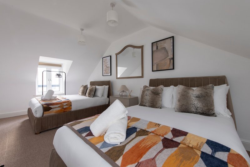Twin bedroom with two beds, neutral upholstery, patterned blankets, wall art and skylight window