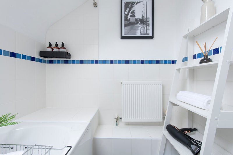 Clean white bathroom with blue tile border, bathtub, radiator, and white shelving unit