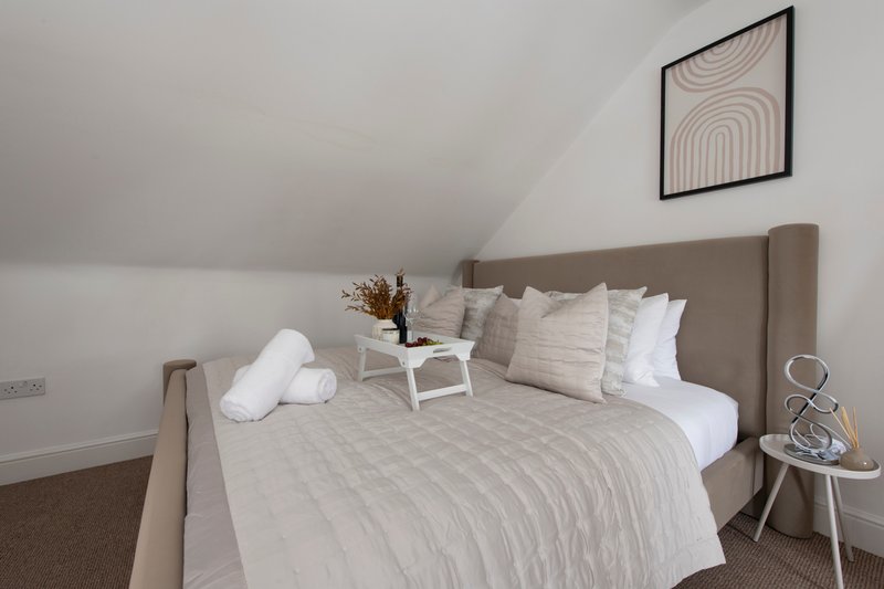 Modern bedroom with upholstered bed, white pillows, geometric wall art, and side table