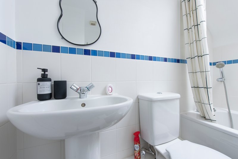 Modern bathroom with white sink, toilet, blue tile border, mirror and shower enclosure