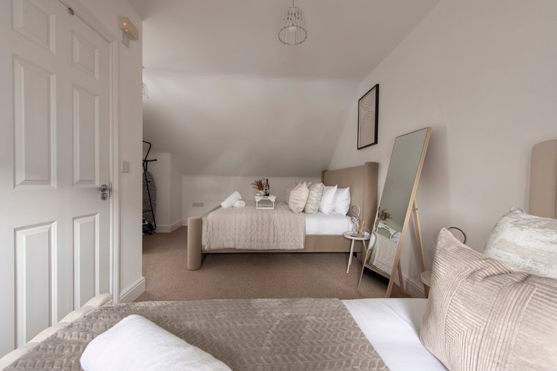 Spacious bedroom with multiple beds, neutral decor, mirrors, and wooden flooring throughout